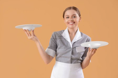 Hermosa joven camarera con platos vacíos sobre fondo beige