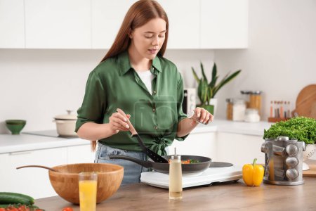 Young woman peppering fried vegetables in kitchen