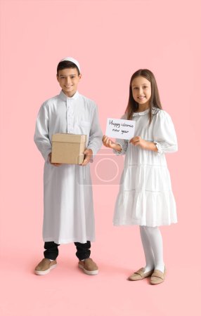 Pequeños niños musulmanes con tarjeta de felicitación para el Año Nuevo Islámico y regalo sobre fondo rosa