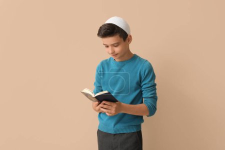 Little Muslim boy with Quran on beige background