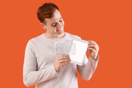 Glücklicher junger Rotschopf mit Tablette auf orangefarbenem Hintergrund