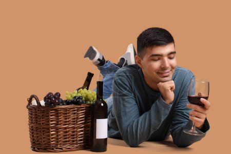 Photo for Young man with wine and basket lying on beige background - Royalty Free Image