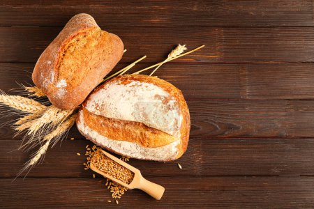Photo for Loaves of fresh bread, wheat spikelets and grains on wooden background - Royalty Free Image