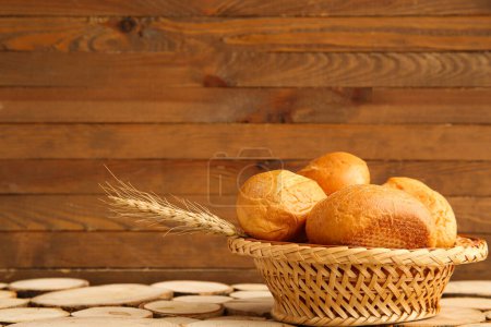 Photo for Wicker basket with loaves of fresh bread and wheat spikelets on wooden background - Royalty Free Image