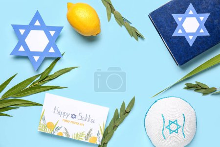 Sukkot festival composition with frame made from four species (lulav, hadas, arava, etrog), Torah and greeting card on blue background