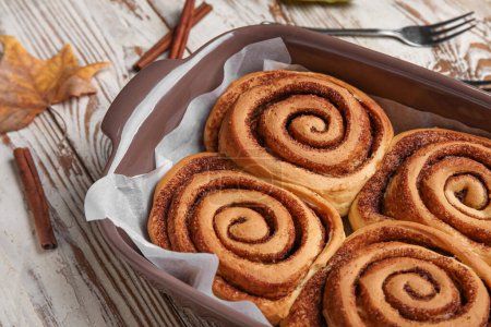 Baking dish of tasty cinnamon rolls on white wooden background