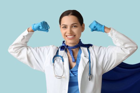 Beautiful female doctor in superhero costume showing muscles on blue background
