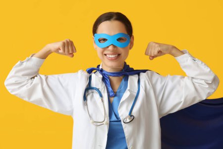 Belle femme médecin en costume de super-héros montrant les muscles sur fond jaune