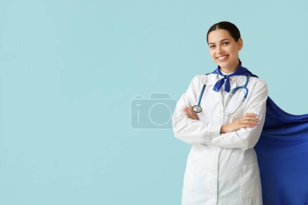 Beautiful female doctor in superhero costume on blue background