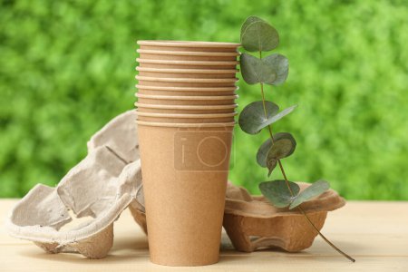 Foto de Vajilla ecológica con rama de planta sobre mesa de madera beige contra hierba verde decorativa - Imagen libre de derechos