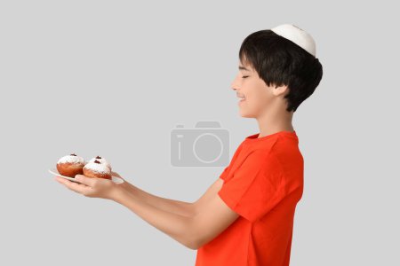 Photo for Little boy in kipa holding plate with tasty donuts on grey background. Hanukkah celebration - Royalty Free Image
