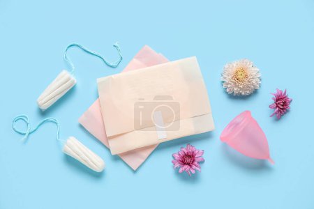 Téléchargez les photos : Coupe menstruelle avec tampons, tampons et fleurs sur fond bleu - en image libre de droit