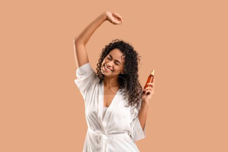 Beautiful African-American woman with hair spray on beige background