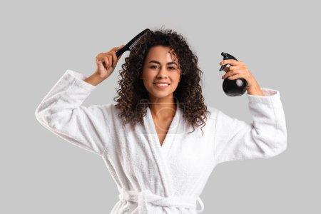 Beautiful African-American woman with hair spray and comb on light background