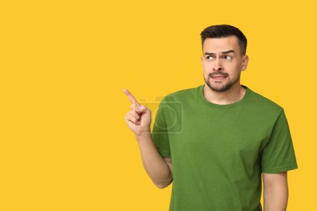 Téléchargez les photos : Beau jeune homme honteux pointant quelque chose sur fond jaune - en image libre de droit