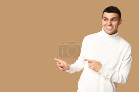 Handsome ashamed young man pointing at something on brown background