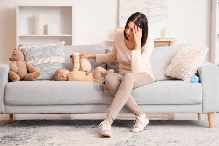 Junge Frau mit Spielzeug und ihrem an postnataler Depression leidenden Baby auf dem heimischen Sofa