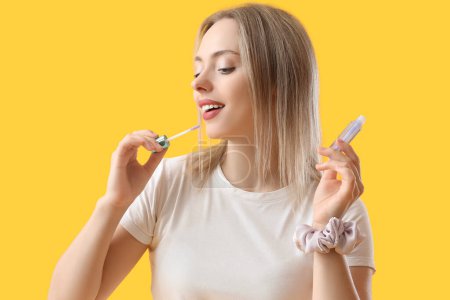 Young blonde woman with scrunchy and lip gloss on yellow background, closeup