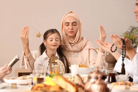 Happy Muslim mother with her little daughter praying before dinner at home. Ramadan celebration