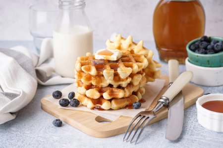 Wooden board of tasty waffles with blueberries and maple syrup on white background