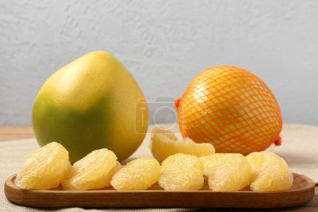 Foto de Sabrosos frutos de pomelo enteros y plato de madera con piezas sobre fondo claro - Imagen libre de derechos