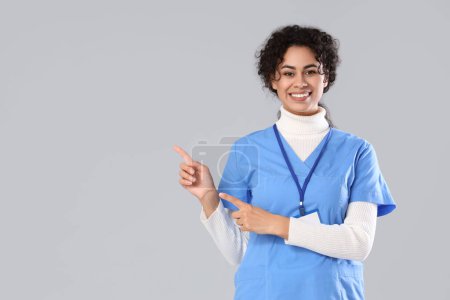 Female African-American medical intern pointing at something on light background
