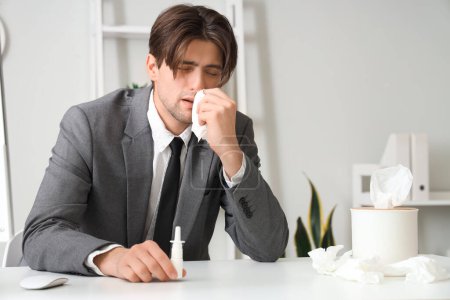 Téléchargez les photos : Homme d'affaires malade avec des gouttes nasales et des éternuements de tissus au bureau - en image libre de droit