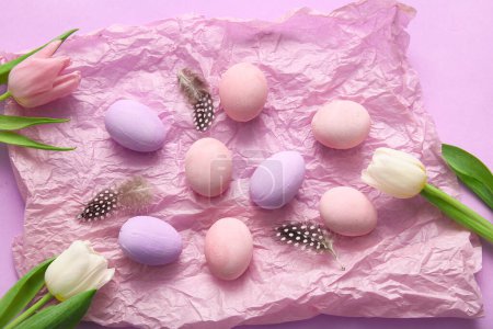 Téléchargez les photos : Papier froissé avec des œufs de Pâques peints, des plumes et des fleurs de tulipes sur fond violet - en image libre de droit