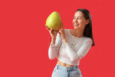 Foto de Mujer joven sonriente con pomelo sobre fondo rojo - Imagen libre de derechos