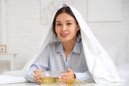 Photo for Young Asian woman with towel doing steam inhalation at table in bedroom - Royalty Free Image
