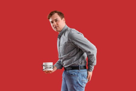 Young man with barbed toilet paper on red background. Hemorrhoids concept