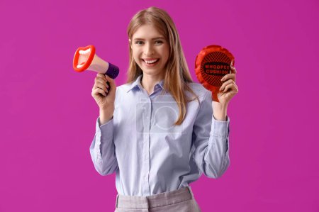 Young businesswoman with whoopee cushion and megaphone on purple background. April Fools' Day celebration