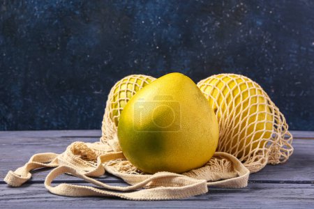 Foto de Bolso de cuerda con frutas frescas de pomelo sobre mesa de madera azul - Imagen libre de derechos