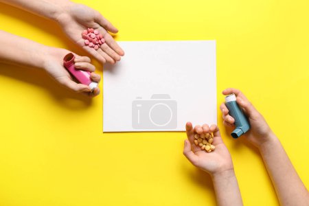 Téléchargez les photos : Mains de l'enfant avec carte blanche, pilules et inhalateurs d'asthme sur fond jaune - en image libre de droit