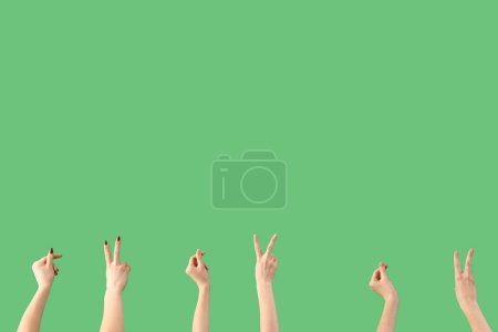 Foto de Manos femeninas mostrando gestos de paz y sosteniendo algo sobre fondo verde - Imagen libre de derechos