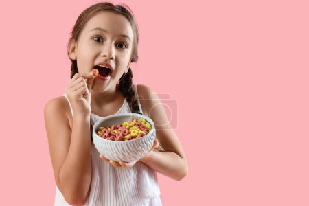 Petite fille mignonne mangeant des anneaux de céréales sur fond rose