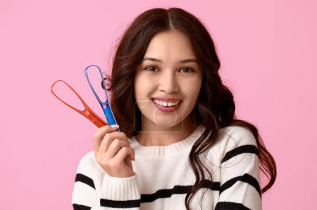 Young Asian woman with tongue scrapers on pink background