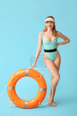 Schöne junge Frau im Panzer-Badeanzug und mit Rettungsring auf blauem Hintergrund