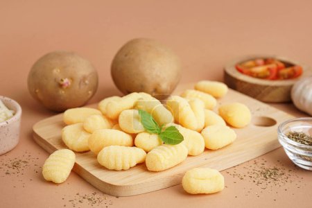 Wooden board with tasty gnocchi and spices on beige background, closeup
