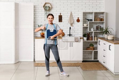 Téléchargez les photos : Jeune femme avec des balances de poids et ruban à mesurer montrant pouce à la maison. Concept minceur - en image libre de droit