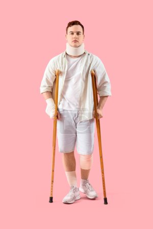 Verletzter junger Mann nach Unfall mit Krücken auf rosa Hintergrund