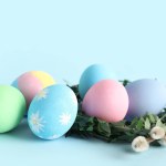 Green nest with painted Easter eggs and willow branch on blue background