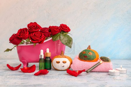 Téléchargez les photos : Citrouille avec des visages dessinés, des fournitures de spa, des roses et des masques en argile sur table bleue grunge - en image libre de droit
