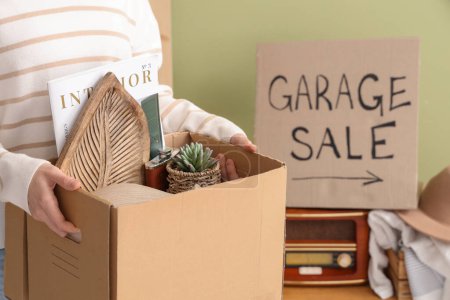 Téléchargez les photos : Femme tenant boîte de choses indésirables pour la vente de garage dans la chambre - en image libre de droit