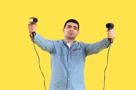 Photo for Handsome young man with hair dryers on yellow  background - Royalty Free Image