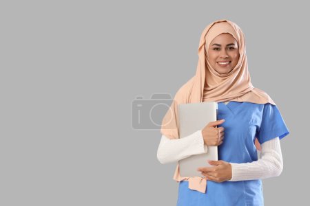 Female Muslim medical intern with laptop on light background