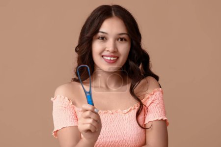 Happy young Asian woman with tongue scraper on brown background