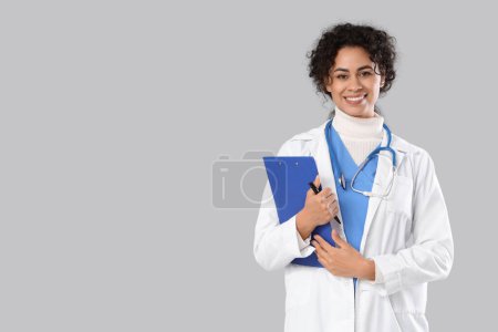 Female African-American medical intern with clipboard on light background