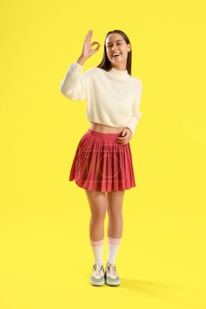 Téléchargez les photos : Jeune femme montrant OK sur fond jaune - en image libre de droit