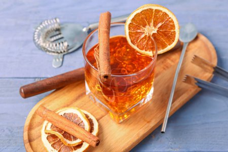 Board with glass of delicious Old Fashioned Cocktail and orange slices on purple wooden background